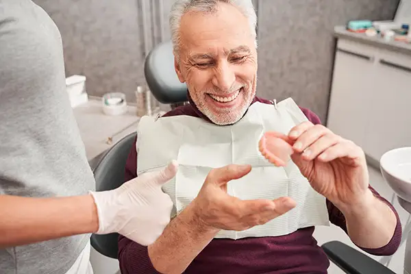 Elderly male patient smiling and examining a set of dentures at Karl Hoffman Dentistry in Lacey, WA